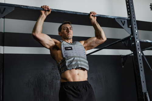 male athlete doing chest-to-bar pull-ups wearing weighted vest